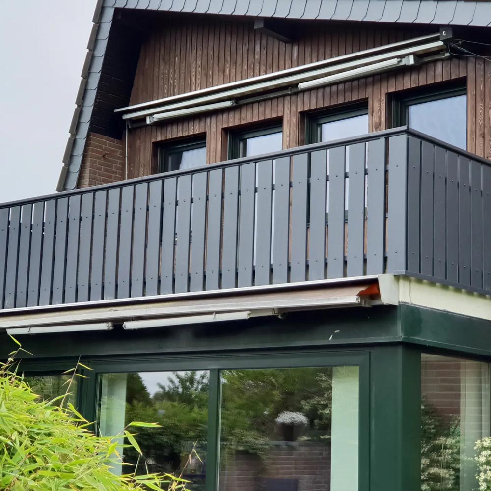 Zweistöckiges Haus mit dunkelgrauem Balkon, Holzfassade und markanter Überdachung.