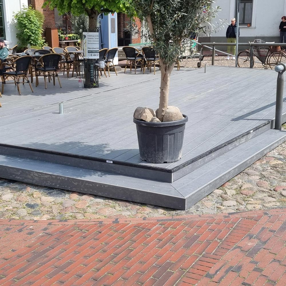 Eine erhöhte Holzterrasse mit Blumentopf und Steinen, umgeben von Sitzgelegenheiten.