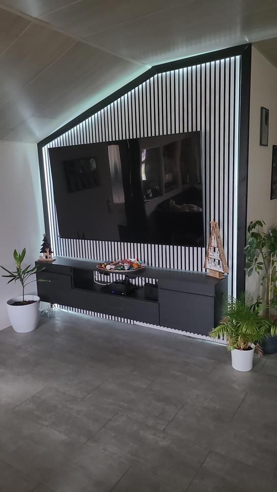 Wohnzimmer mit großem TV an gestreifter Wand, dekoriert mit Pflanzen und Weihnachtsbaum.