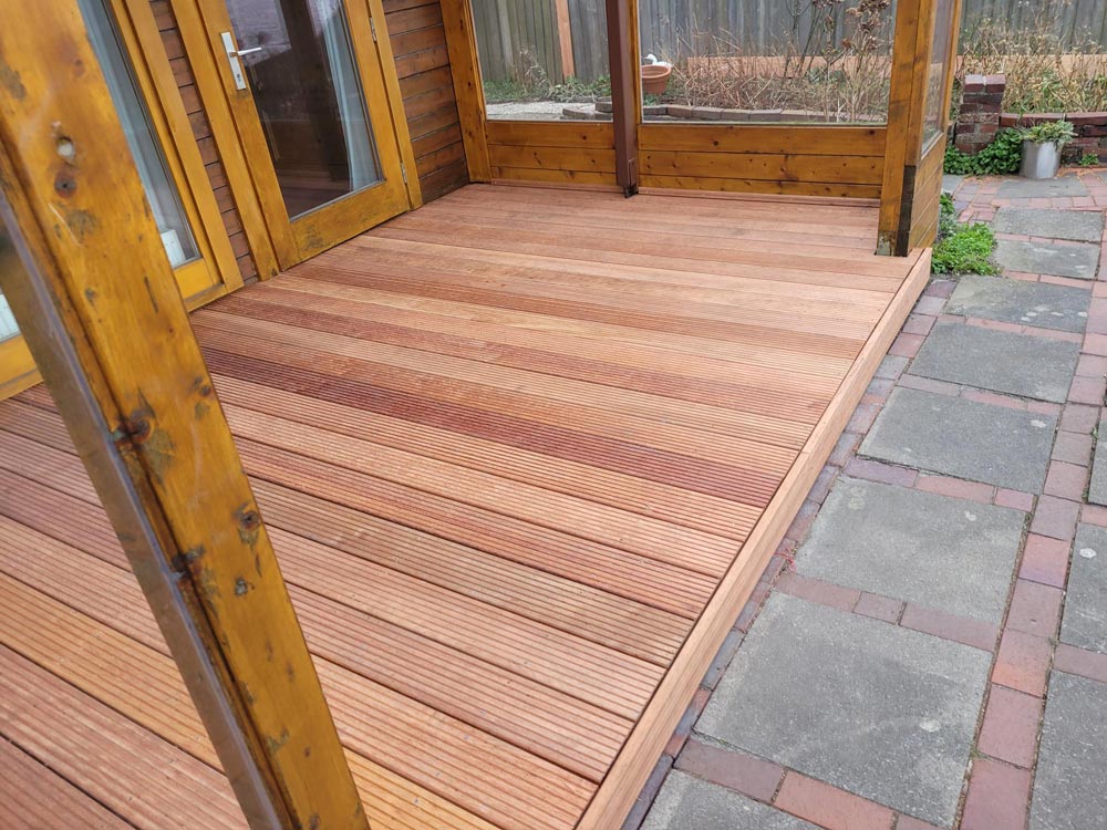 Frisch verlegte hölzerne Terrasse mit klaren Linien, angrenzend an ein Haus mit hölzerner Verkleidung.