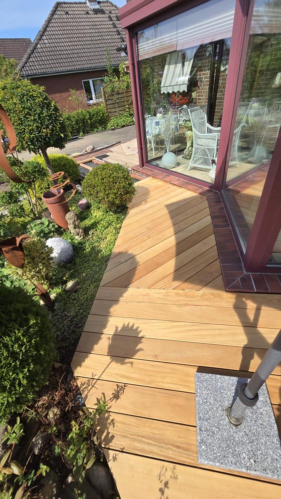 Holzterrasse mit Garten; Glaserker, grüner Rasen, stilvolle Pflanzen und dekorative Keramiktöpfe.